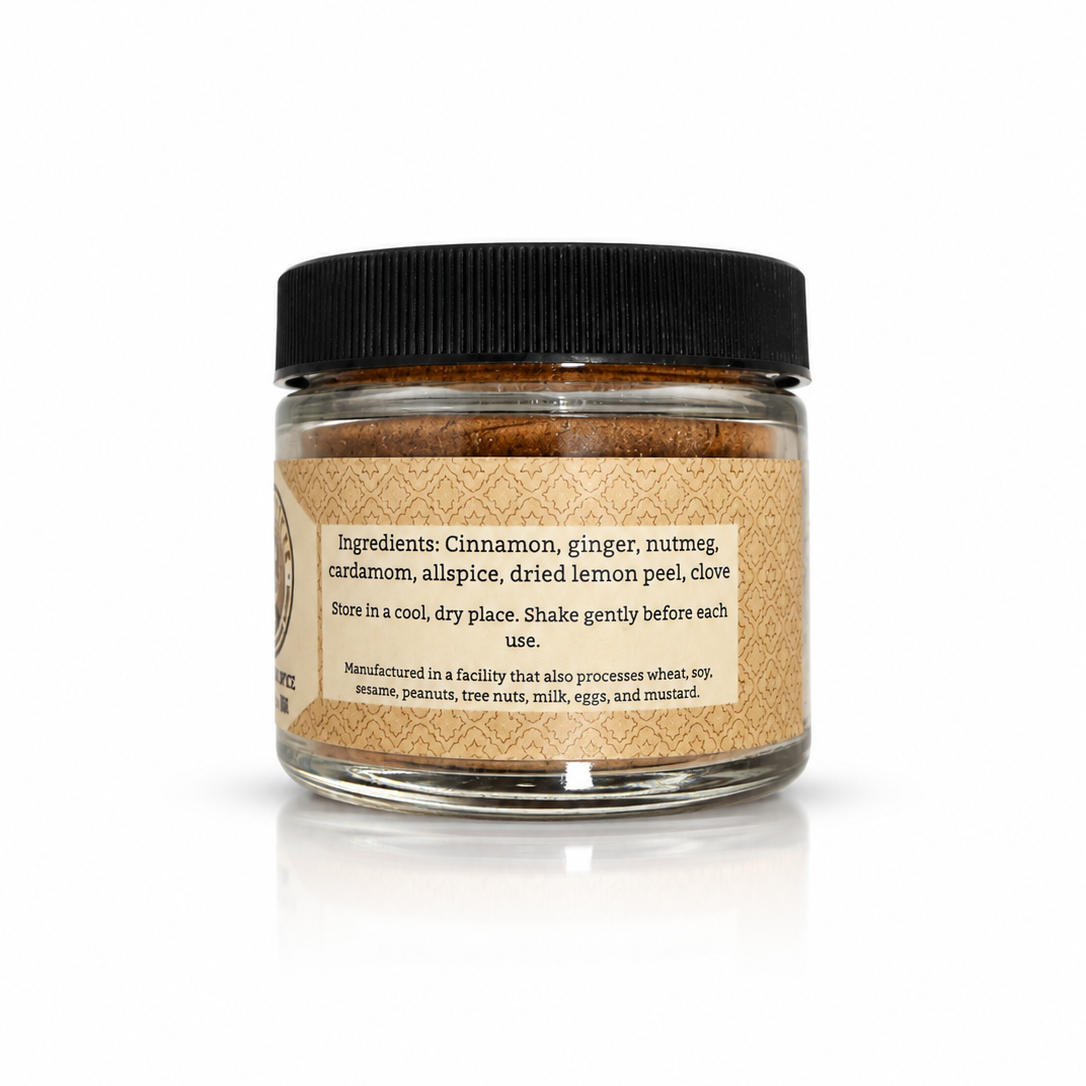 A small clear jar of Savta's Spices Apple Cake Spice blend with a black screw-top lid and a tan paper label, photographed on a clean white background with a soft reflection below.