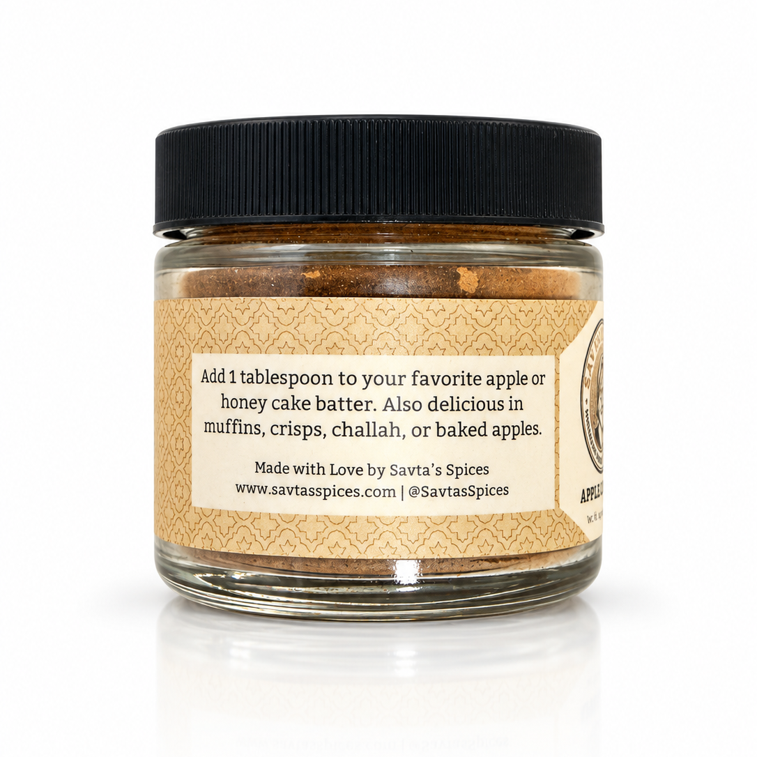 A jar of Savta's Spices Apple Cake Spice blend with a black lid and a beige label, shown on a white background with a soft reflection.