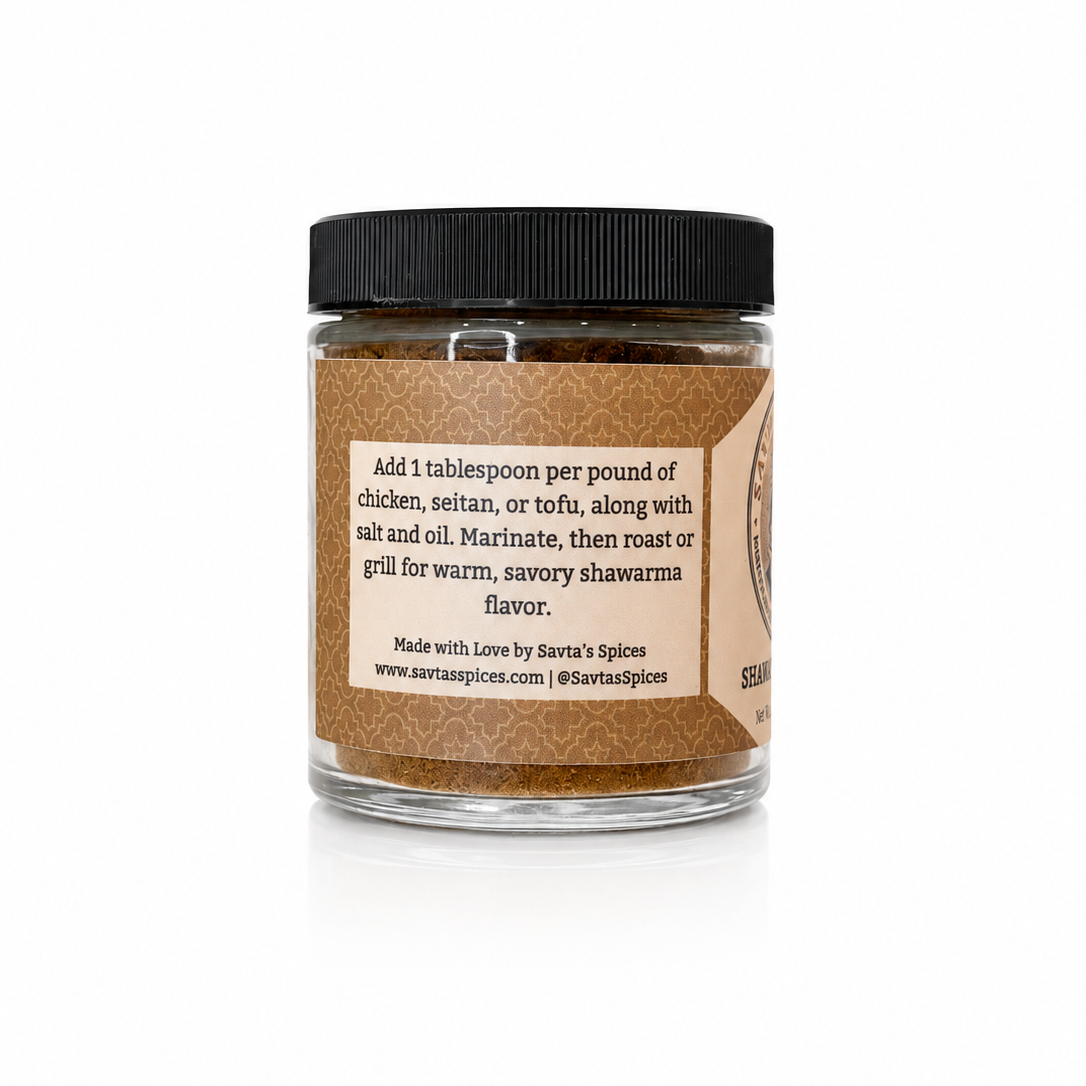 A clear glass jar of Savta's Spices brown spice blend with a black lid and a brown paper label, shown on a white background with a soft reflection.