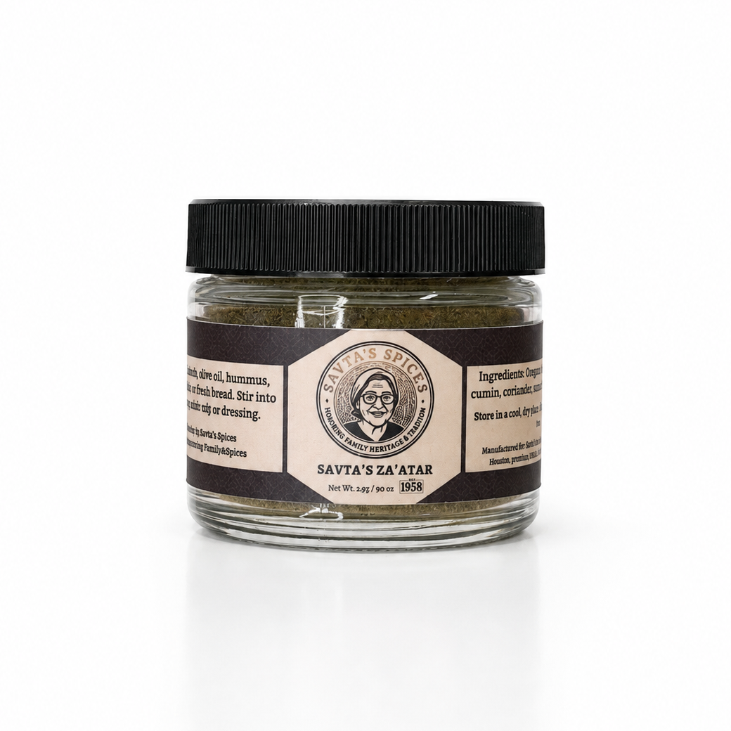 A small clear glass jar containing dark green Savta's Za'atar spice paste, sealed with a black ribbed lid and featuring a brown and cream paper label with a portrait illustration.